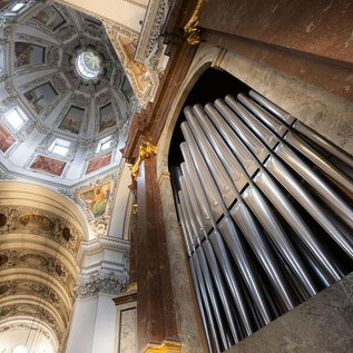 Imponujący organ kościelny z błyszczącymi rurami. Wzrok kieruje się na artystycznie zaprojektowany sufit kościoła. | © Dom zu Salzburg