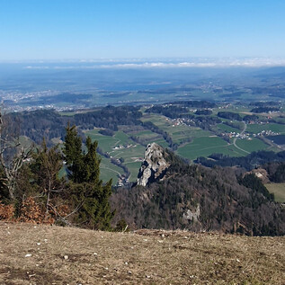 Eine malerische Landschaft mit grünen Feldern und Bergen. Im Vordergrund ist ein auffälliger Felsen zu sehen. | © Sylvia Wienerroither