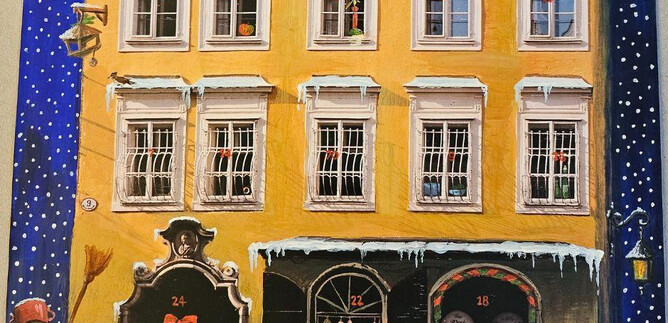 Una vista festiva de la ciudad con la casa natal de Mozart en amarillo. Delante del edificio hay un muñeco de nieve y una pequeña decoración navideña. | © ISM