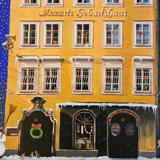 Une vue festive de la ville avec la maison natale de Mozart en jaune. Devant le bâtiment se tiennent un bonhomme de neige et une petite décoration de Noël. | © ISM