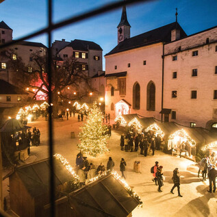 Ein festlicher Weihnachtsmarkt mit einem geschmückten Baum und beleuchteten Ständen. Viele Menschen genießen die Atmosphäre an einem klaren Abend. | © Burgen und Schlösser