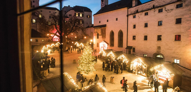 Ein festlicher Weihnachtsmarkt mit einem geschmückten Baum und beleuchteten Ständen. Viele Menschen genießen die Atmosphäre an einem klaren Abend. | © Burgen und Schlösser