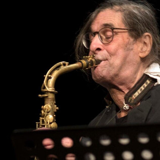 Starší hudebník hraje na saxofon na scéně. Má brýle a dlouhé vlasy. | © J.P. Sonntag