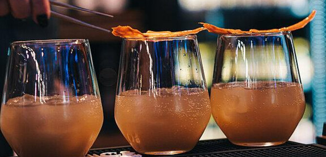 Drei Cocktails in eleganten Gläsern stehen auf einer Bar. Eine Person dekoriert sie mit getrockneten Früchten. | © Messezentrum Salzburg