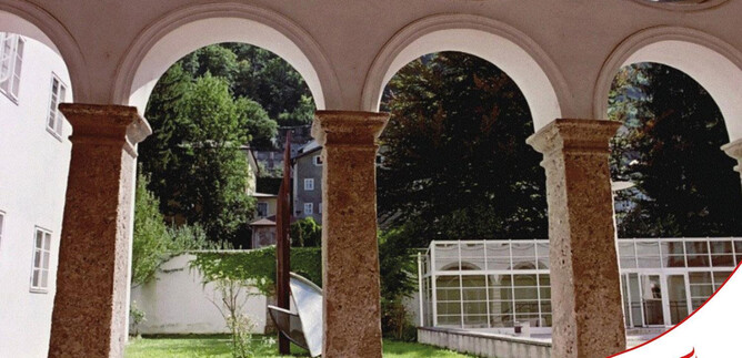 A courtyard with large arches and green grass. In the background, trees and a greenhouse can be seen. | © Kultur Tourismus