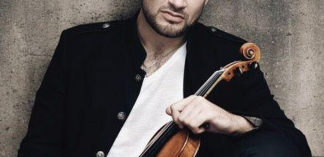 A man is sitting with a violin in his hand. He is wearing a black jacket and is looking seriously at the camera. | © recreation Event GmbH