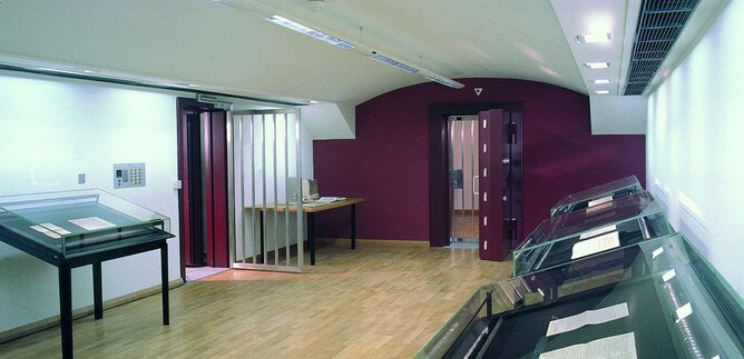 A modern exhibition space with large display cases. Walls in bright white and dark red, and natural wood flooring create an inviting atmosphere. | © ISM