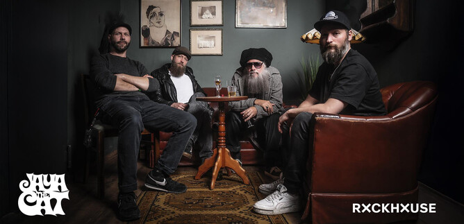 Eine Gruppe von vier Männern sitzt in einer gemütlichen Ecke mit einem Holzstuhl und einem Tisch. Die Wand ist dunkel gestrichen und mit Kunstwerken dekoriert. | © Photo Jockey