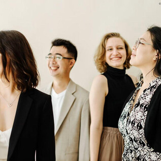 Un grupo de cuatro personas está junto y sonríe.  
Llevan diferentes y elegantes conjuntos, lo que crea una atmósfera amigable y relajada. | © Theresa Pewal