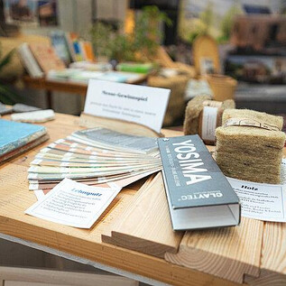 A wooden table with various materials and information cards. Below are color samples, books, and natural materials for use in construction projects. | © Messezentrum Salzburg