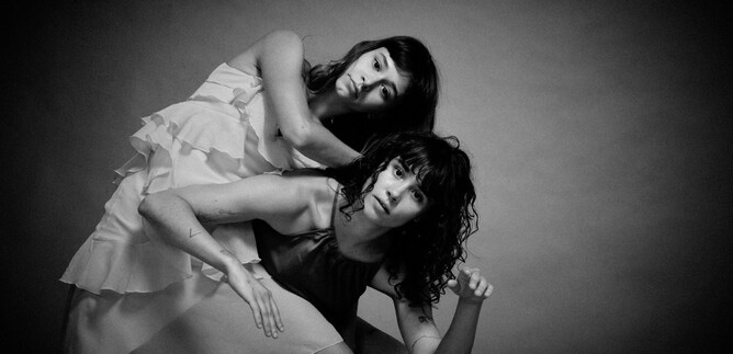 Two women pose artistically in black and white. They have expressive facial expressions and wear different dresses. | © Chris Rogl