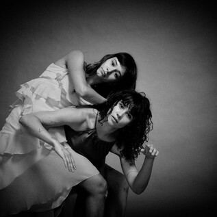 Dvě ženy umělecky pózují v černobílé. Mají výrazné výrazy obličeje a nosí různé šaty. | © Chris Rogl