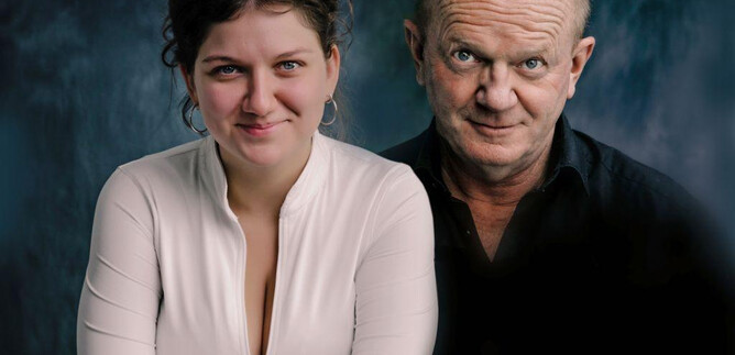 A portrait of two people sitting next to each other. The woman has curly hair and is wearing a white top, the man has short hair and is wearing a black shirt. | © Christian Hartmann