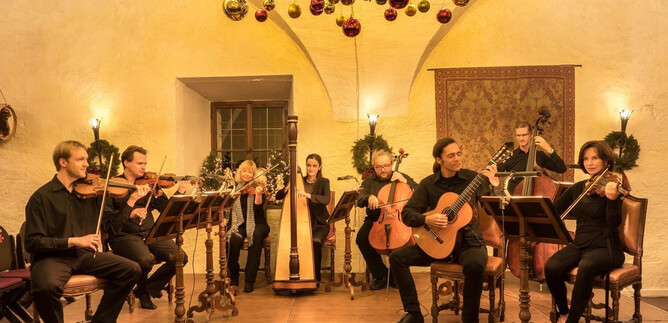 A musical performance in a festively decorated room. Several musicians are playing different instruments while sitting on chairs. | © Salzburg Highlights