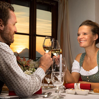 A romantic dinner at sunset. A man and a woman toast with glasses, while cozy table decor is visible in the background. | © Salzburg Highlights