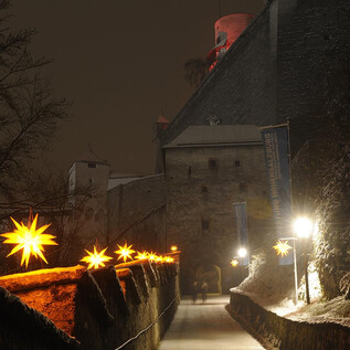 A castle at night, surrounded by snow.  
Glowing stars adorn the path to the castle. | © Salzburger Burgen und Schlösser