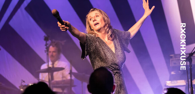 A singer passionately performs on stage. In the background, a musician plays the drums. | © Martin Hüttler