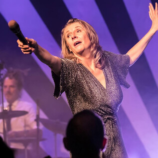 Zpěvačka vášnivě vystupuje na scéně. V pozadí hraje hudebník na bicí. | © Martin Hüttler