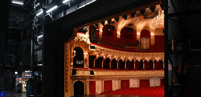 Ein Blick hinter die Bühne eines Theaters mit roten Sitzen und einer eleganten Einrichtung. Die Bühne ist beleuchtet und zeigt prächtige Details. | © Neumayr_Leo