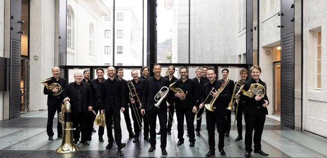 A group of musicians with brass instruments is standing in a modern room. They are wearing black clothing and smiling at the camera. | © Mozarteumorchester Salzburg
