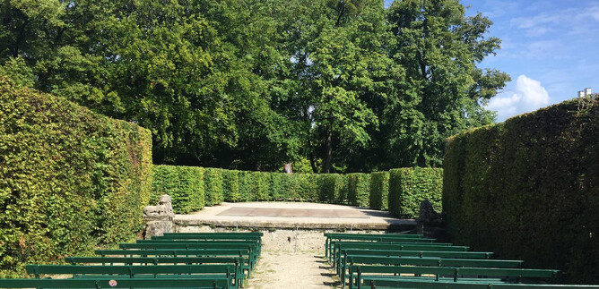 An open-air stage surrounded by tall hedges and benches. The sky is clear and the surroundings feel inviting. | © Tourismus Salzburg