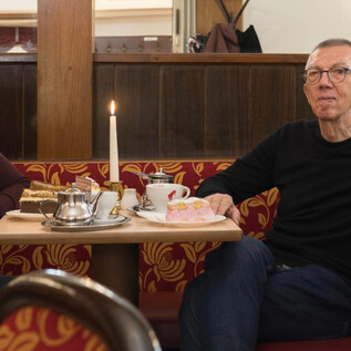 A couple is sitting at a table in a cozy café. On the table are cakes, a candle, and cups with drinks. | © Wolfgang Lienbacher