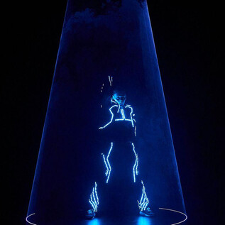 Eine Person in einem leuchtenden Anzug steht in einer transparenten Kuppel. Sie strahlt in blauen Lichtern und sorgt für einen futuristischen Effekt. | © Foto Flausen