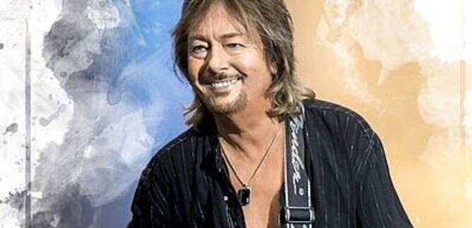 A musician with a guitar is smiling at the camera. The background is artistically designed with colors. | © YEA Sp. z o.o