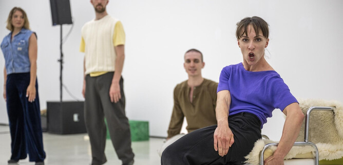 Four dancers are standing in a bright room. The focus is on a dance pose of a woman in a blue shirt. | © Bernhard Müller