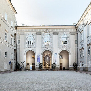 Ein schöner Innenhof mit historischer Architektur. Die Wände sind hell, und in der Mitte befindet sich ein dekorierter Eingang. | © DomQuartier