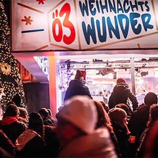 A festive Christmas market scene with many people. In the background, there stands a beautifully decorated Christmas tree and a colorful booth with the sign "Christmas Miracle." | © Martin Krachler_oe3.orf.at
