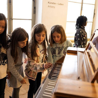 Un grupo de chicas mira con curiosidad un piano y se ayuda mutuamente. Parecen divertirse explorando las teclas. | © Erika Mayer