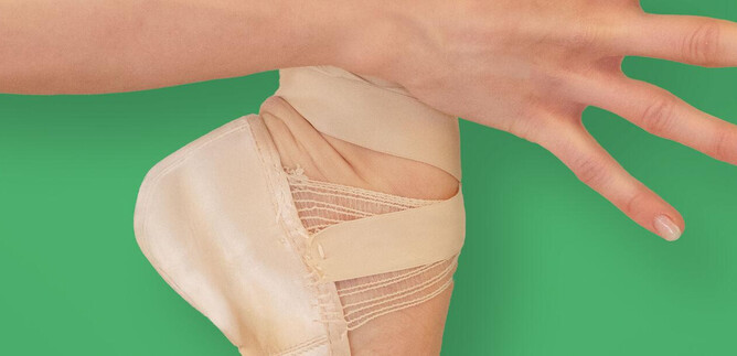 A hand holds a ballet shoe with elastic straps. The background is green. | © Salzburger Landestheater