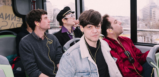 A group of four young people is sitting in a bus. They are listening to music and looking out the window. | © Ingo Pertramer