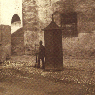 Historické místo se kamennou zdí a malou, nad ní stojící strukturou. Osoba stojí v popředí vedle strážní věže.