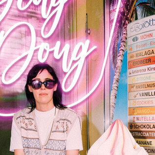 Eine Person sitzt vor einem leuchtenden Neon-Schild mit dem Text "Belly Doug". Neben ihnen befindet sich ein Menü mit verschiedenen Eissorten. | © Ingo Pertramer