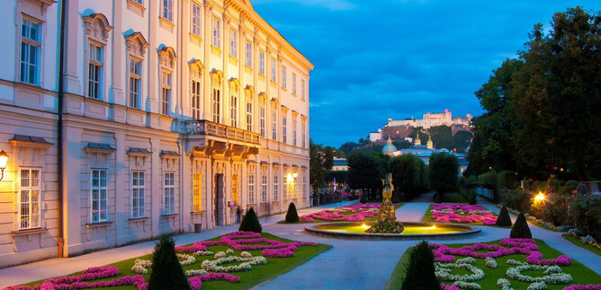 Ein wunderschöner Garten mit bunten Blumen und gepflegten Rasenflächen. Im Hintergrund ist ein historisches Gebäude und eine Burg zu sehen. | © Salzburger Konzertgesellschaft