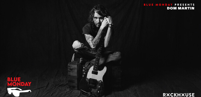 Ein Mann sitzt auf einer Kiste und hat eine E-Gitarre in der Hand. Er trägt ein schwarzes Outfit und schaut nachdenklich in die Kamera. | © Rob Blackham
