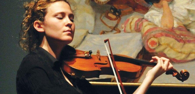 Une femme joue passionnément du violon devant une peinture. Elle porte un haut noir et a des cheveux bouclés. | © Frank Stewart