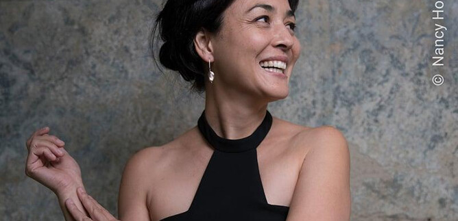 Une femme avec un sourire joyeux porte un haut noir. Son regard est dirigé vers le haut, tandis qu'elle pose élégamment. | © Nancy Horowitz