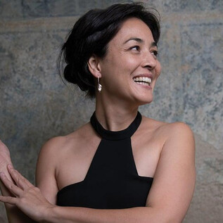 Žena s radostným úsměvem nosí černý top. Její pohled je směřován vzhůru, zatímco elegantně pózuje. | © Nancy Horowitz