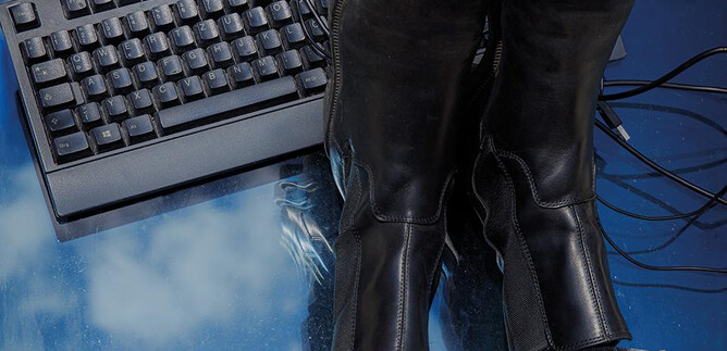 Black boots are lying on a table with a keyboard and a computer mouse. Many cables are visible. | © Valentina Schuster