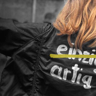 A person is wearing a black jacket with a striking lettering on the back. The text “unique” is partially crossed out. | © Eva-Maria Spiß