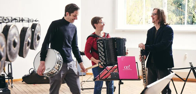 Tre musicisti stanno in una stanza luminosa e suonano strumenti diversi. Uno suona l'accordeon, mentre gli altri tengono un tamburo e un strumento a fiato. | © Andreas Hechenberger