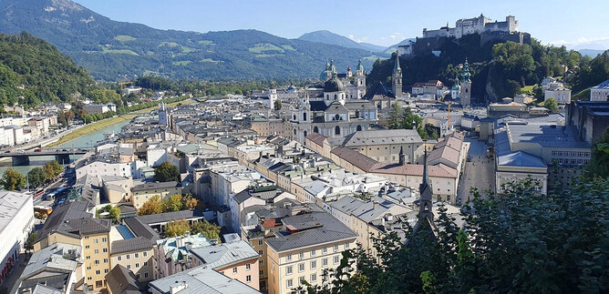 Una vista pintoresca de la ciudad de Salzburgo con edificios históricos y la fortaleza Hohensalzburg al fondo. Las montañas y el cielo azul completan el hermoso paisaje. | © Wienerroither Sylvia