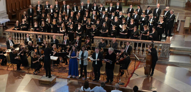 Un coro canta in una chiesa, circondato da musicisti. L'atmosfera è festosa e musicale. | © Dom zu Salzburg