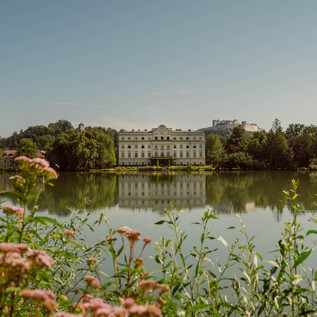 An elegant castle reflects in the calm lake. Surrounded by lush greenery and colorful flowers. | © TSG Tourismus Salzburg GmbH, Patrick Langwallner