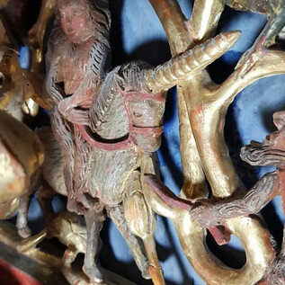 Eine kunstvolle Holzschnitzerei zeigt eine Figur auf einem Einhorn. Der Hintergrund ist in blauen und goldenen Tönen gehalten. | © Salzburger Burgen und Schlösser