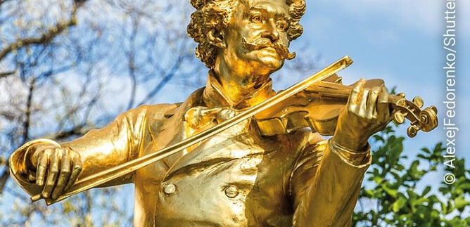 Egy arany szobor egy hegedűs vidáman játssza hangszerét. A háttérben zöld fák és tiszta ég látható. | © AlexejFedorenko/Shutterstock, Moises Patrici