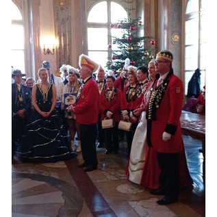 Eine festlich gekleidete Gruppe von Personen steht in einem prunkvollen Raum. Im Hintergrund ist ein Weihnachtsbaum zu sehen. | © Salzburger Faschingsgilde